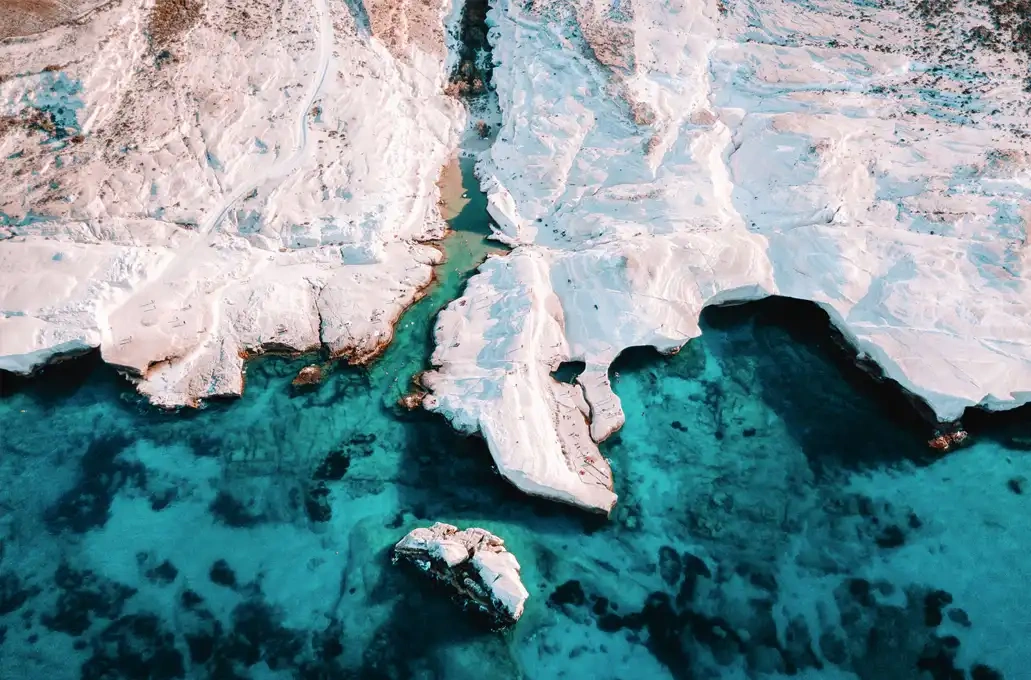 Aerial view of white rocky cliffs and blue waters along a coastline.